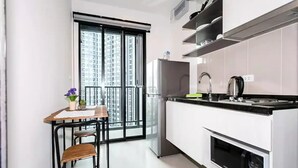 A modern kitchen with a dining area, a refrigerator, a stove, and a window with a view of high-rise buildings.