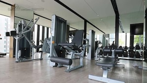 A modern gym with various exercise machines, weight racks, and a bench.