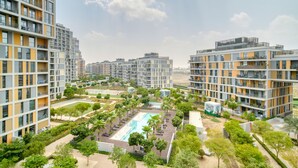 A modern apartment complex with multiple high-rise buildings, a central swimming pool, and landscaped areas with trees.