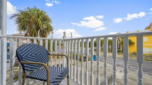 A balcony with a patterned chair, a white railing, and a view of a yellow building and palm tree. - Bright getaway w/ daily tickets & beach access (Panama City Beach)