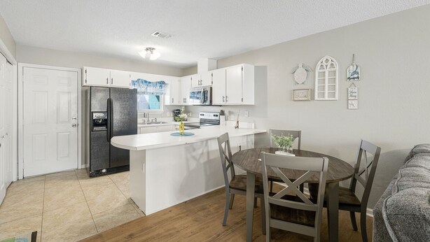 A compact kitchen with white cabinets, a central island, and a dining area with wooden chairs. - Bright getaway w/ daily tickets & beach access (Panama City Beach)