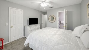 A bedroom with a bed, a ceiling fan, a television on a dresser, and a door leading to another room. - Bright getaway w/ daily tickets & beach access (Panama City Beach)