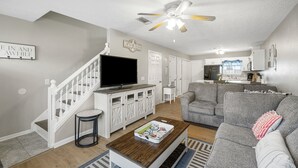A living room with a TV, a grey sofa, a coffee table, and a ceiling fan. - Bright getaway w/ daily tickets & beach access (Panama City Beach)