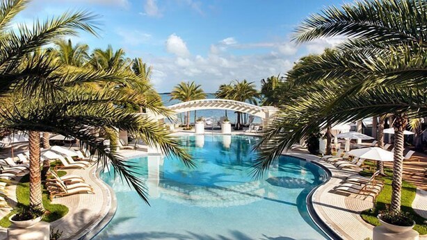 A pool area with lounge chairs, palm trees, and a bridge. - Villa in Key Largo – Gym, Pool + Beach (Key Largo)