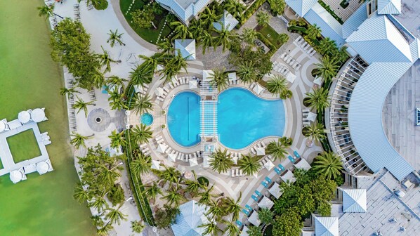 Vista aérea de un resort con piscina central, varias zonas de descanso y palmeras.