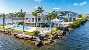 A waterfront property with a swimming pool, palm trees, and a dock.