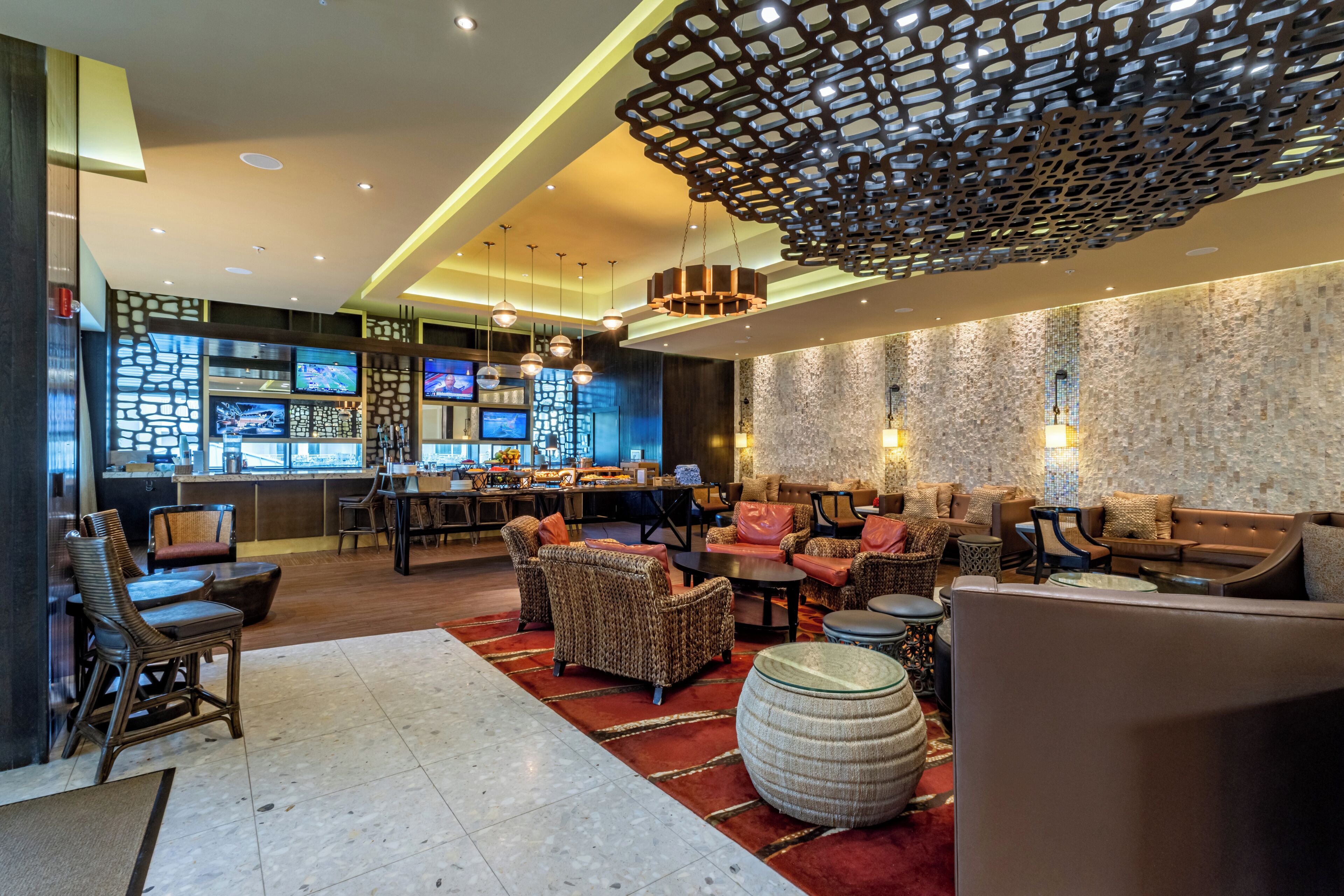Un vestíbulo moderno con zona de bar, arreglos de asientos y un techo decorativo.