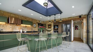 Une cuisine moderne avec des meubles de couleur verte, un îlot central doté de tabourets, un mur d’accent en pierre et une verrière.
