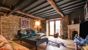 Un salon rustique avec des poutres apparentes, un mur en pierre, une cheminée et une grande fenêtre.