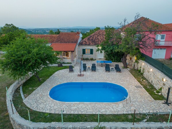 A stone pool surrounded by lounge chairs, a ping pong table, and a stone patio.