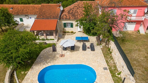 A swimming pool with stone tiles, surrounded by a stone wall, and adjacent to a house with a red-tiled roof. - Villa Rozaria ZadarVillas (Otric)