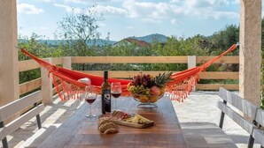 A wooden table set outdoors with a bottle of wine, glasses, a bowl of fruit, and a loaf of bread. - Eden Mediterranean House (Vrsine)