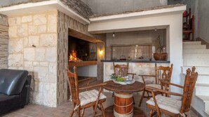 A stone-walled room with a fireplace, a round wooden dining table with chairs, and a black leather sofa. - Eden Mediterranean House (Vrsine)