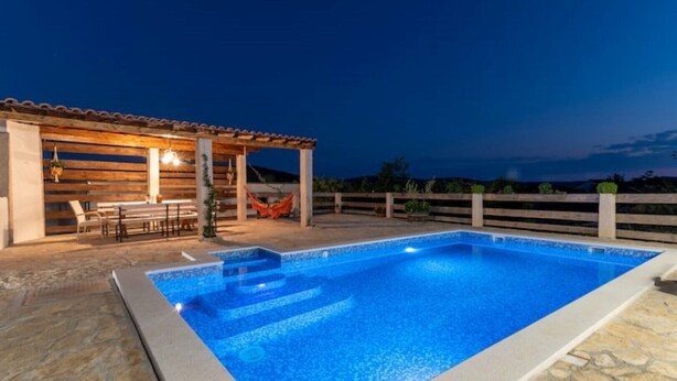 A swimming pool with a wooden deck and a covered seating area. - Eden Mediterranean House (Vrsine)