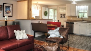 A modern kitchen with white cabinets, a dining area with a red booth, and a living room with a red sofa and leather armchair.