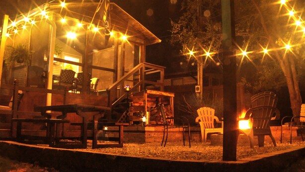 A cozy outdoor seating area with a fire pit, wooden deck, and string lights.