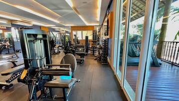 A gym with various exercise machines, a bench, and a view of the outdoors through large windows.