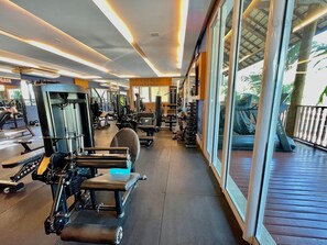 A gym with various exercise machines, a bench, and a view of the outdoors through large windows.