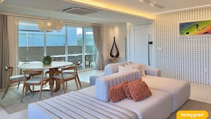 A modern living room with a sofa, a dining table with chairs, and a large window with a view of the outside. - Golf Ville Resort (Aquiraz)