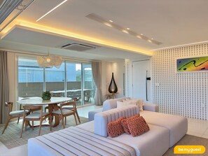 A modern living room with a sofa, a dining table with chairs, and a large window with a view of the outside.