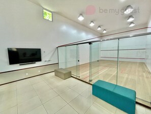 A squash court with glass walls, a television, and a bench.