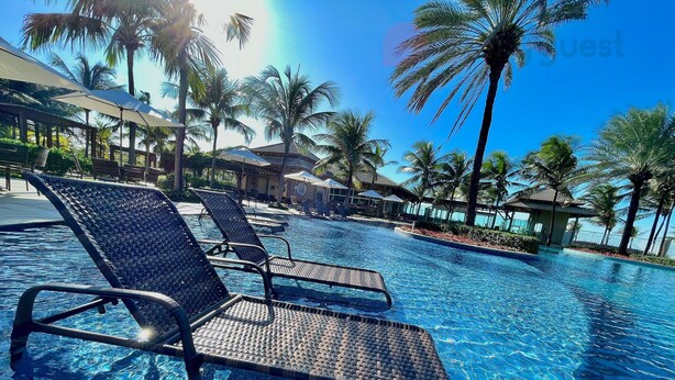 Un área de piscina con sillones de descanso y palmeras.