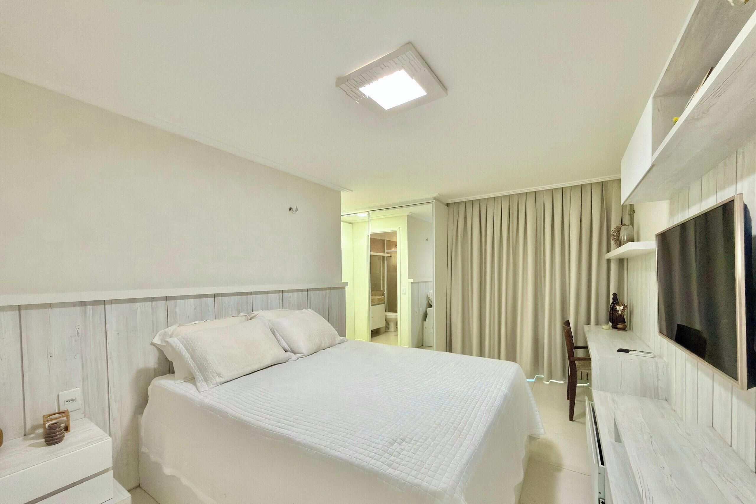 A hotel room with a bed, a TV, a desk, and a bathroom visible through an open door.