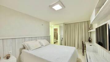 A hotel room with a bed, a TV, a desk, and a bathroom visible through an open door.