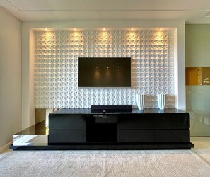Una sala moderna con un televisor de pantalla plana montado en una pared texturizada, un mueble de entretenimiento negro debajo y una alfombra de color claro.