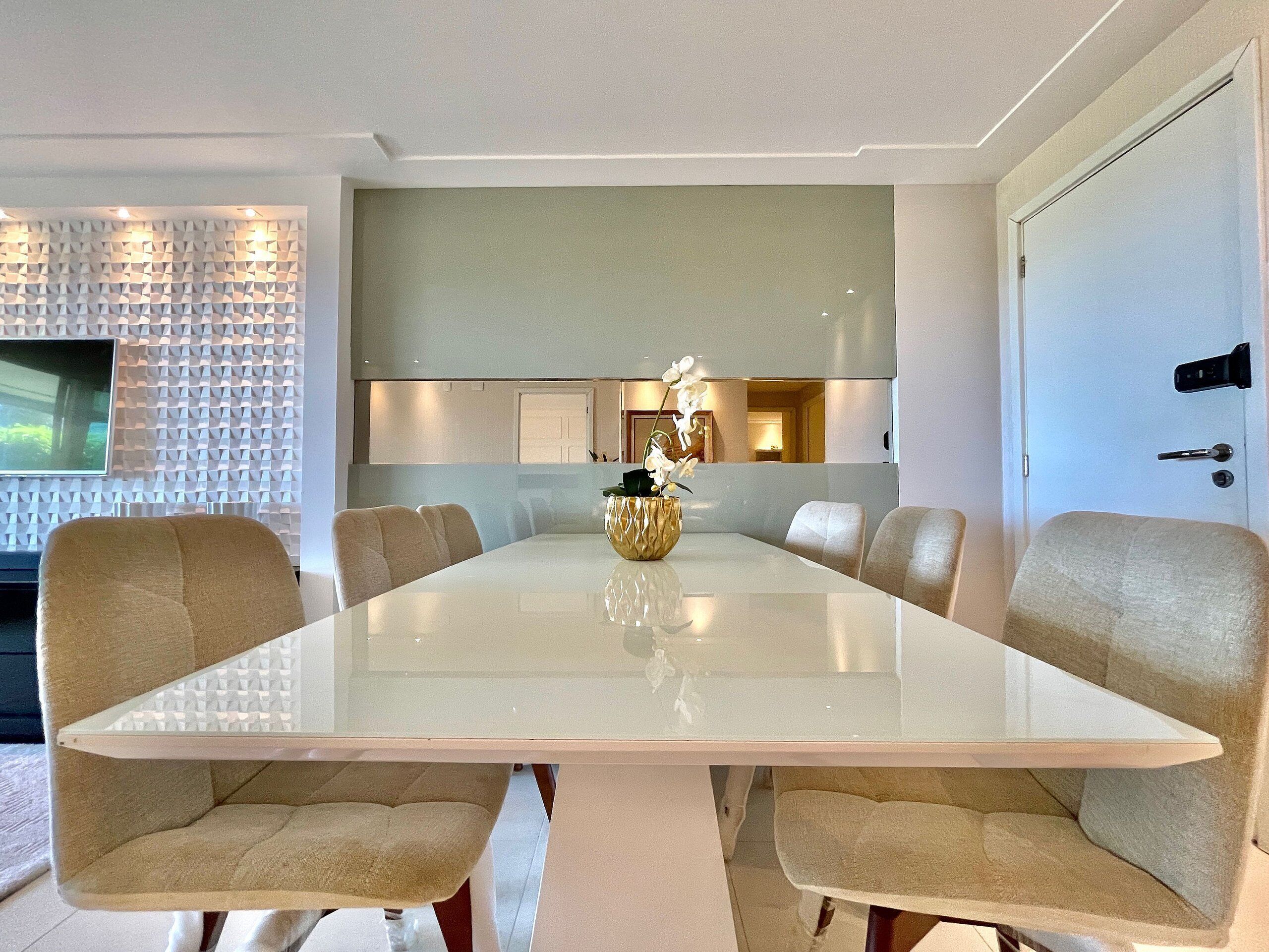 Un comedor moderno con una mesa de vidrio, sillas tapizadas en tono beige y un jarrón decorativo con flores.