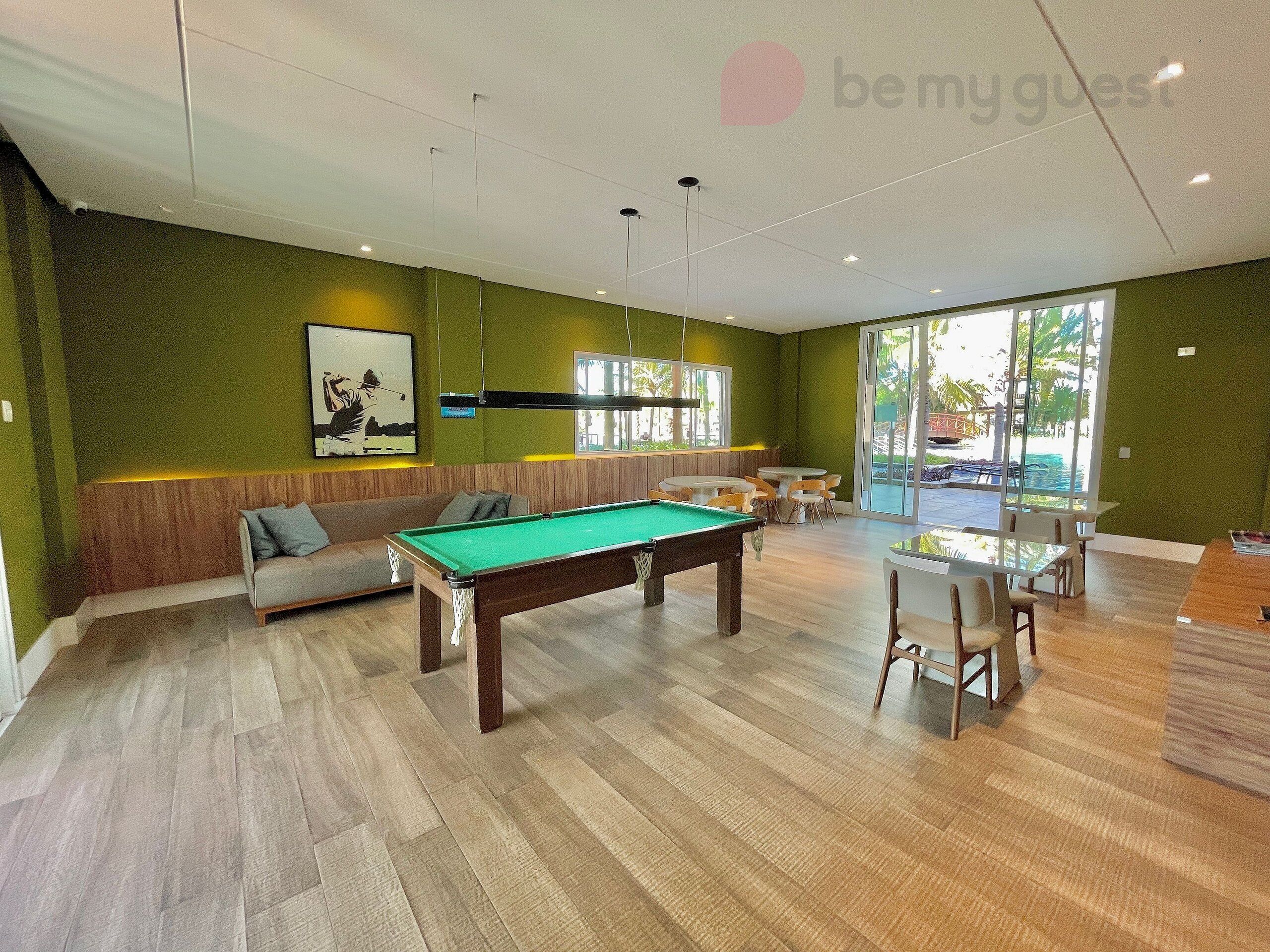 A pool table in a room with a green wall, a sofa, and a dining area.
