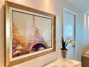 A framed picture of the Eiffel Tower on a wall, a vase with flowers on a marble surface, and a door in the background. - Golf Ville Resort (Aquiraz)