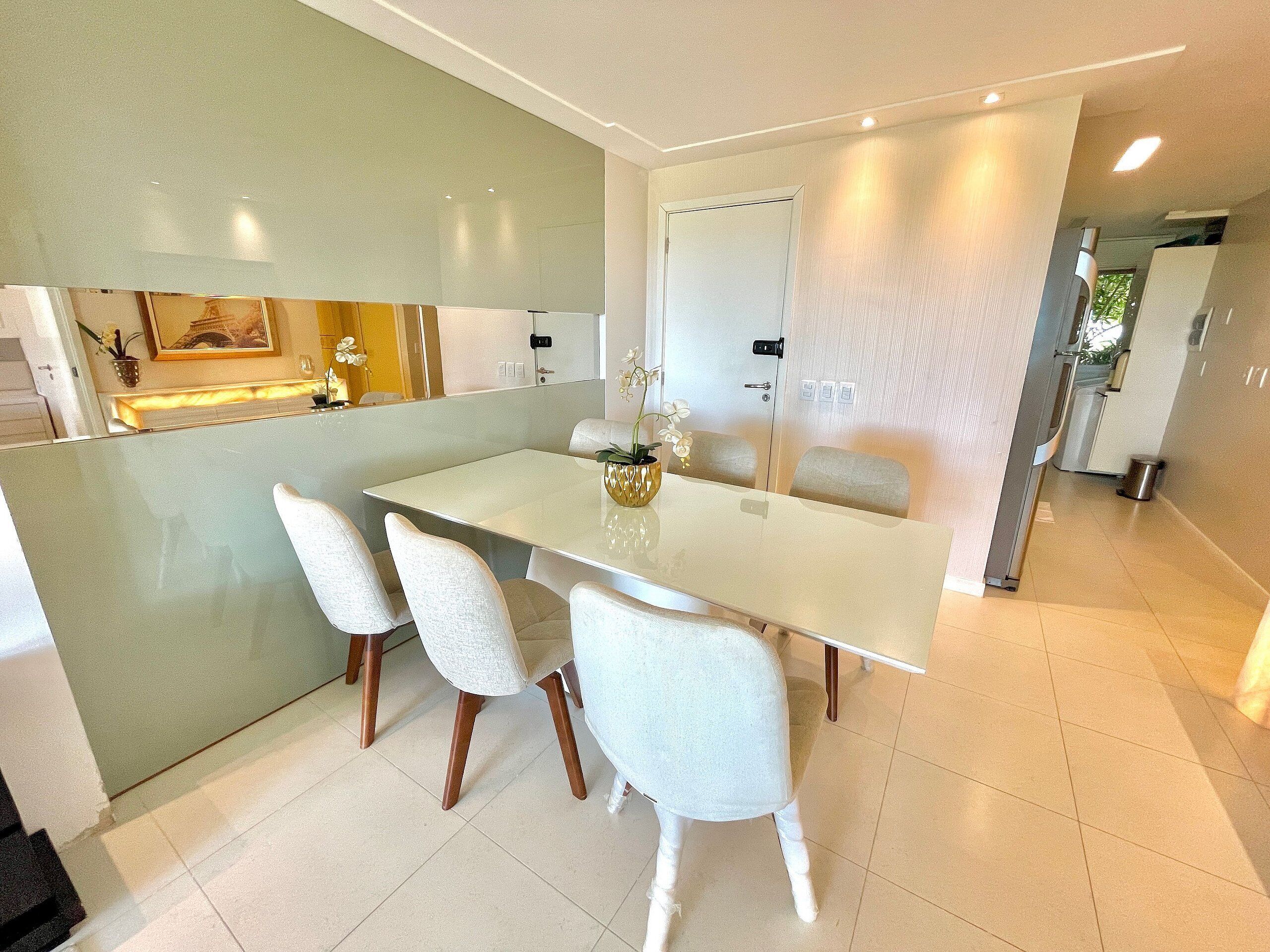 A modern dining area with a white table and chairs, a vase with flowers, and a kitchen in the background.