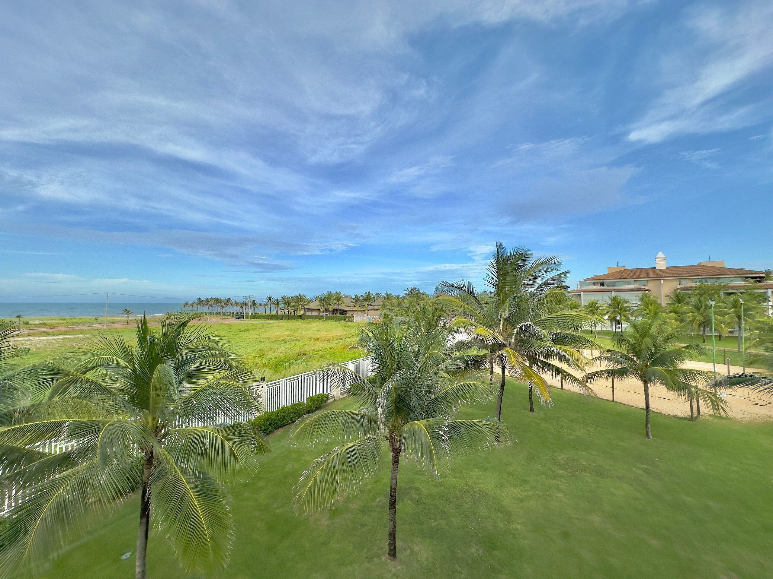 A view of a hotel with a large lawn, palm trees, and a beach in the background.