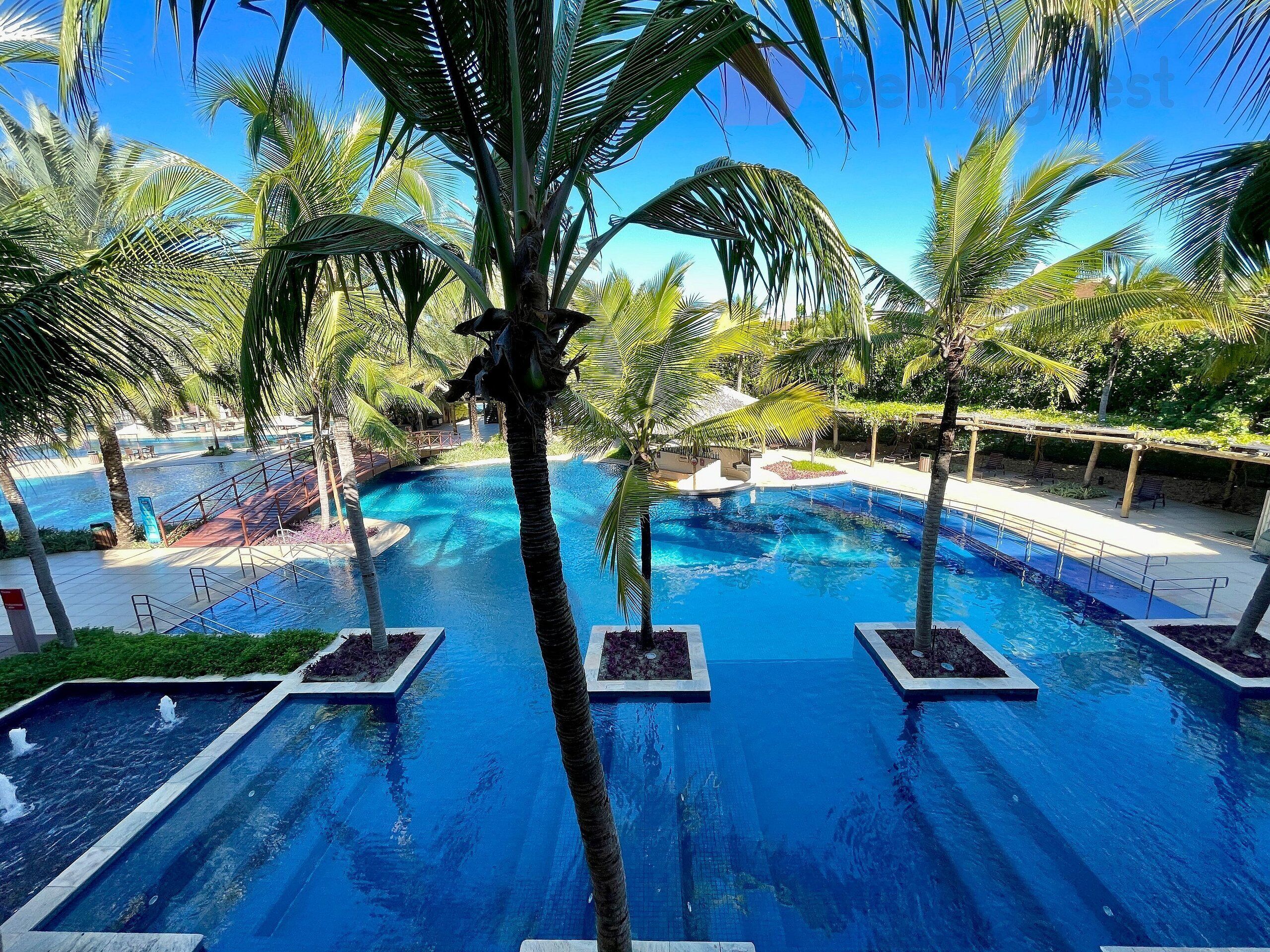Una piscina con varias pistas, rodeada de palmeras y un cielo azul despejado.
