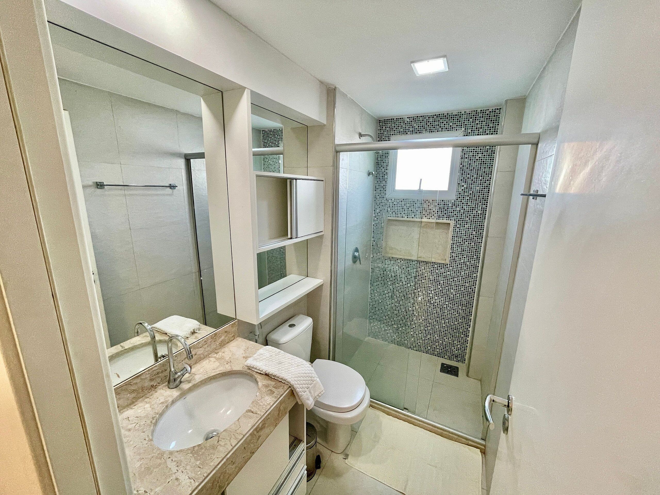A modern bathroom with a glass-enclosed shower, a marble sink, and a toilet.