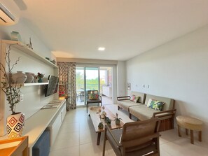A spacious living area with a sofa, chairs, a dining table, and a kitchen counter with decorative items. - Golf Ville Resort (Aquiraz)