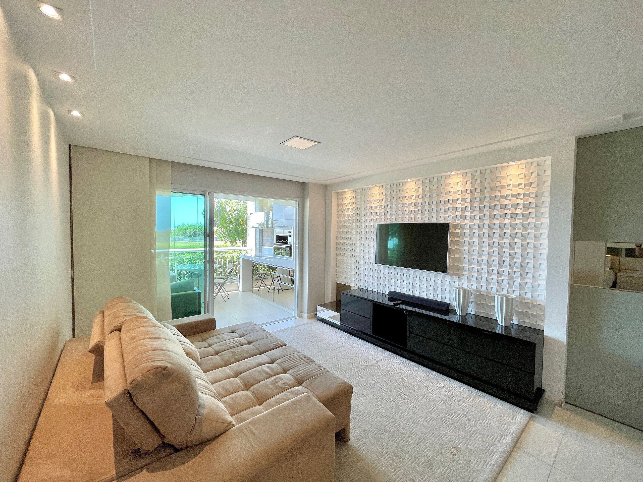 Een moderne woonkamer met een bank, een flatscreen televisie bevestigd aan een gestructureerde muur en een schuifdeur naar een buitenruimte.