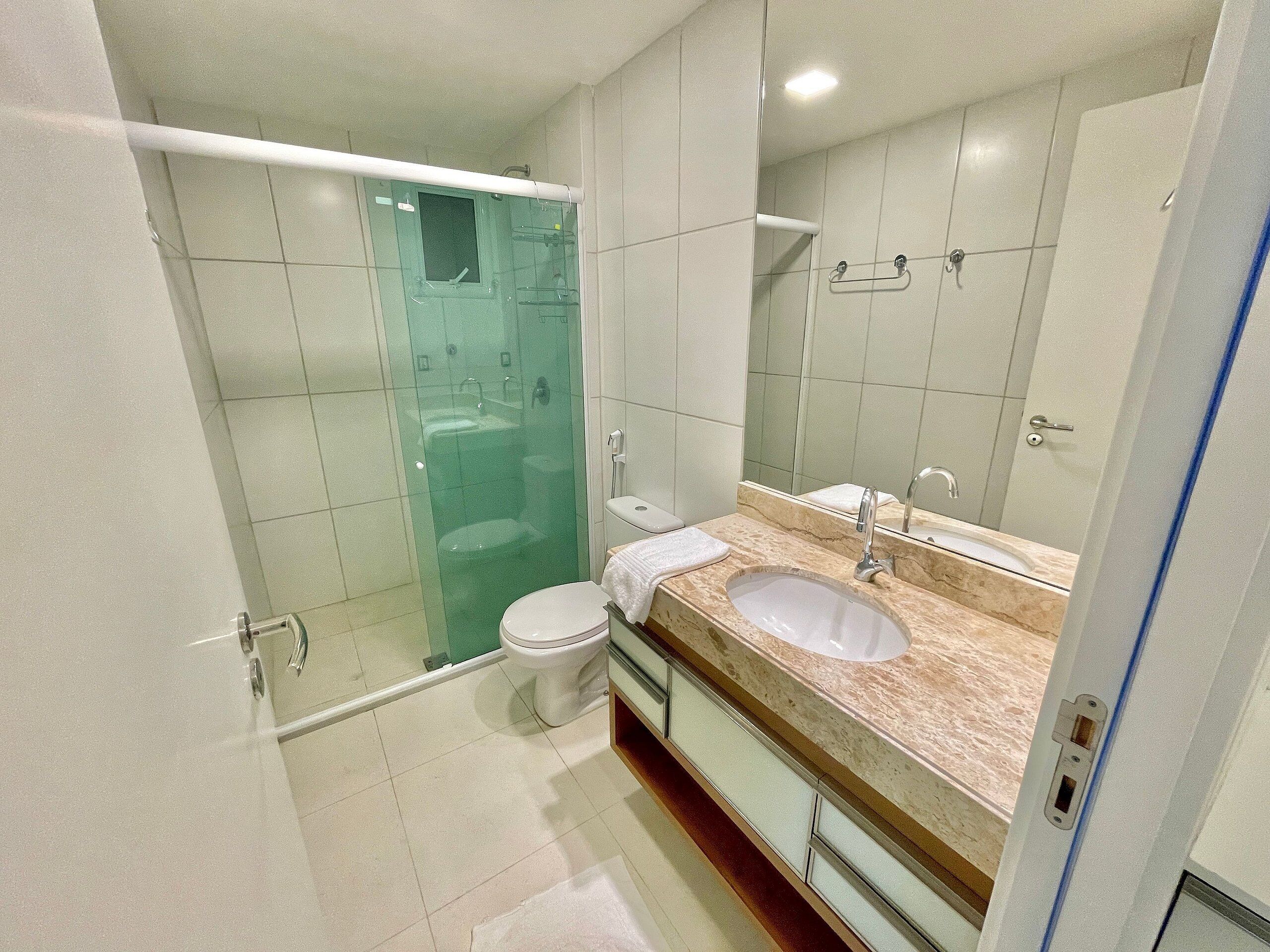 Une salle de bain moderne avec une douche à parois de verre, des toilettes blanches et un lavabo en marbre agrémenté d’un grand miroir.