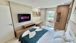 Habitación de hotel con cama, televisor mostrando 'NETFLIX', balcón con mesa y sillas, y armario de madera.
