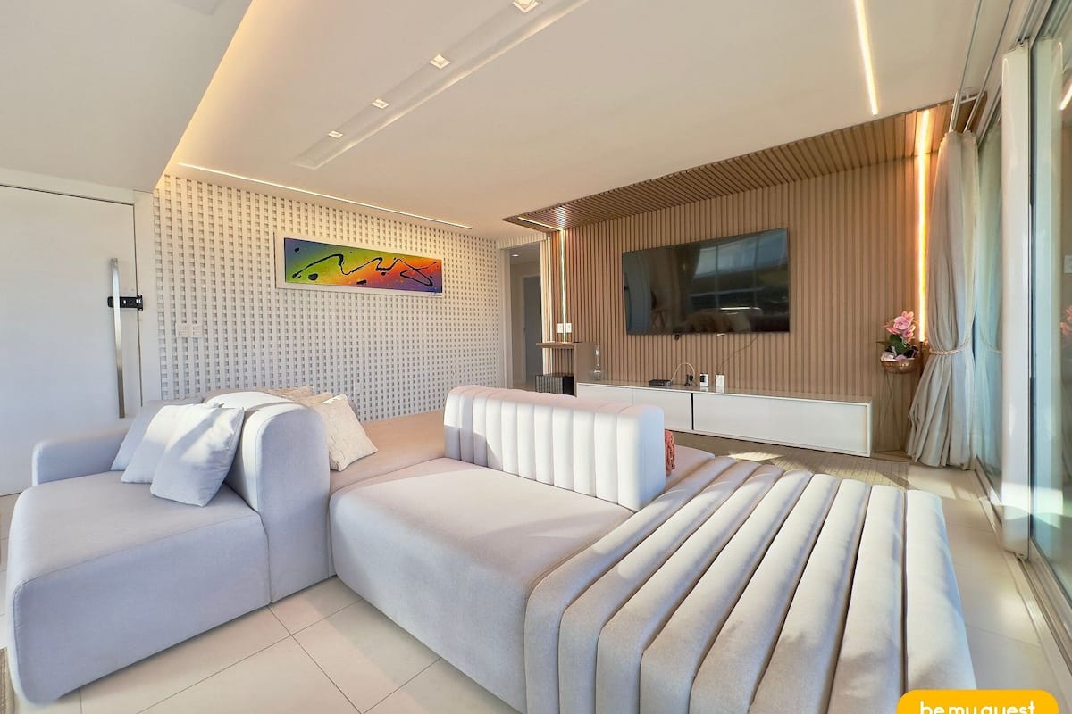 A modern living room with a sectional sofa, a flat-screen TV, and a decorative wall panel.