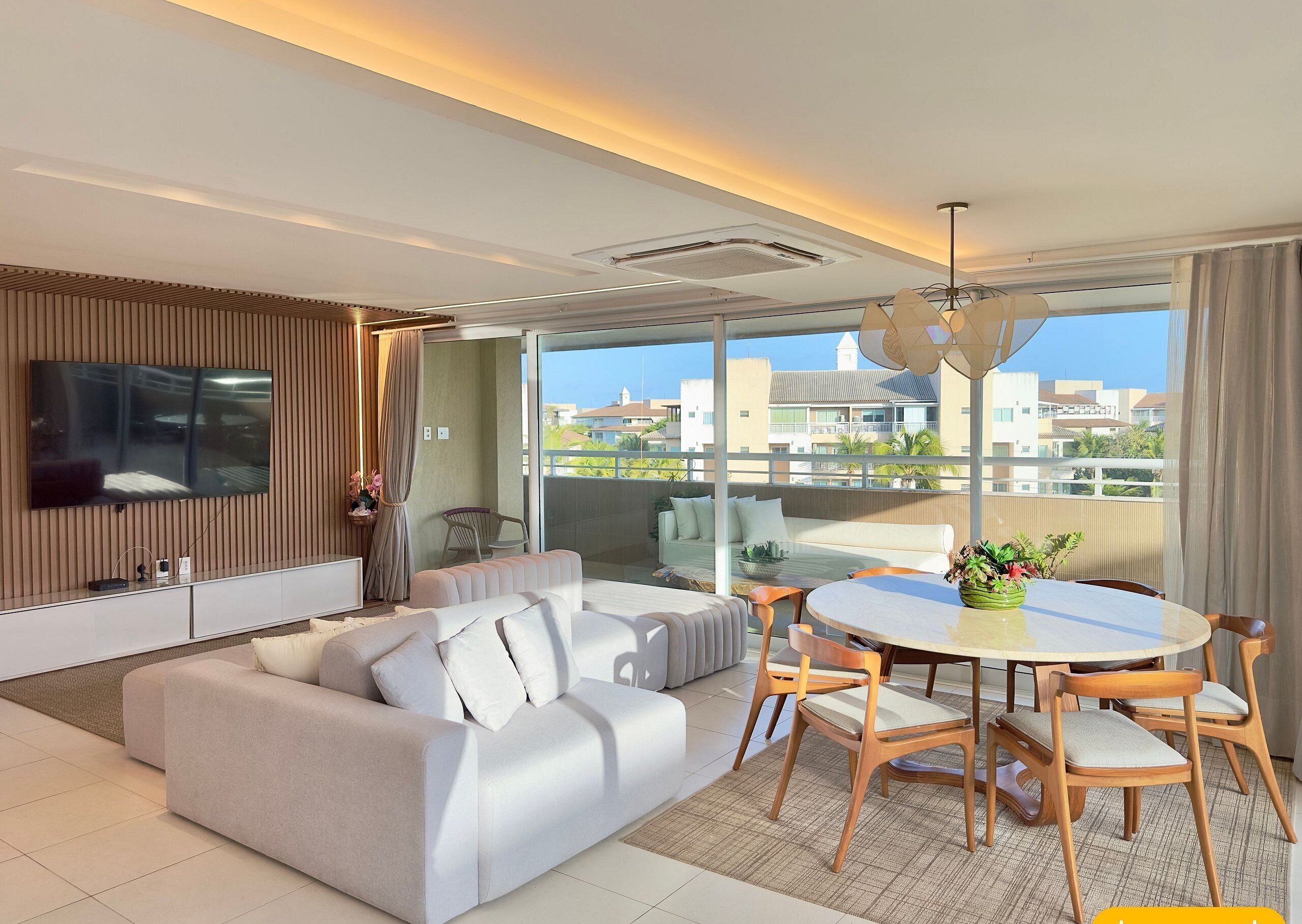 Un salon moderne comprenant un canapé, une table à manger avec des chaises, un téléviseur fixé au mur et un balcon offrant une vue sur les bâtiments.