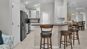 Una cocina moderna con armarios blancos, una isla central con taburetes y un refrigerador empotrado.