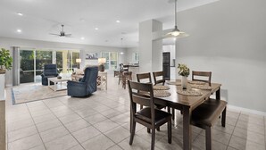 Amplia sala de estar con una mesa de comedor lista para cuatro personas, un sillón azul y un sofá.