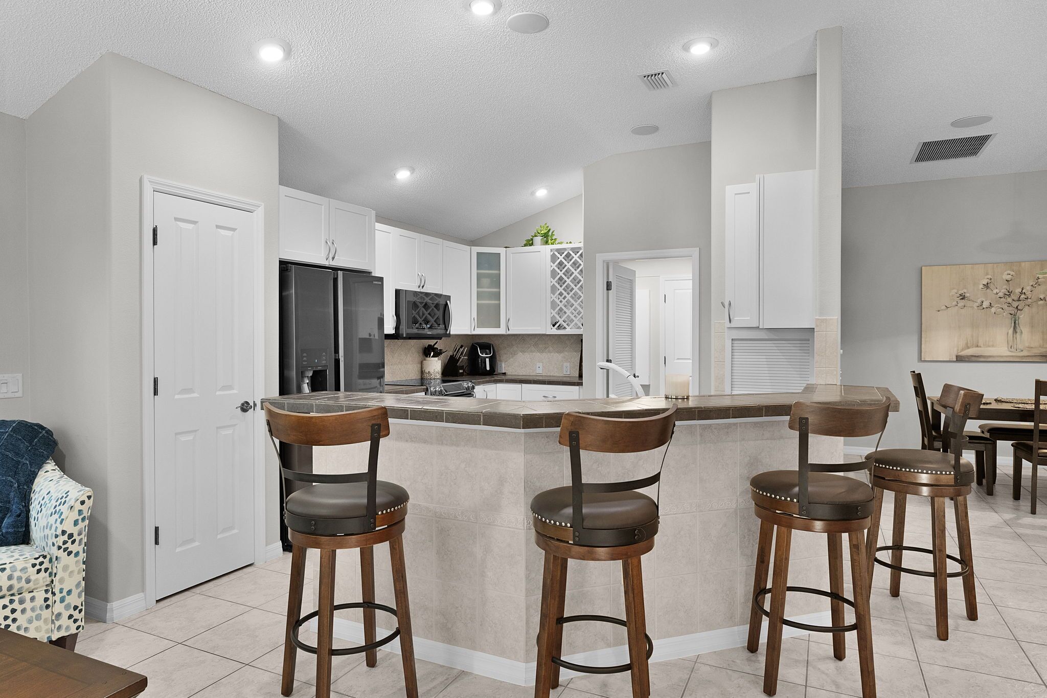 A modern kitchen with white cabinets, a central island with bar stools, a refrigerator, and a microwave.