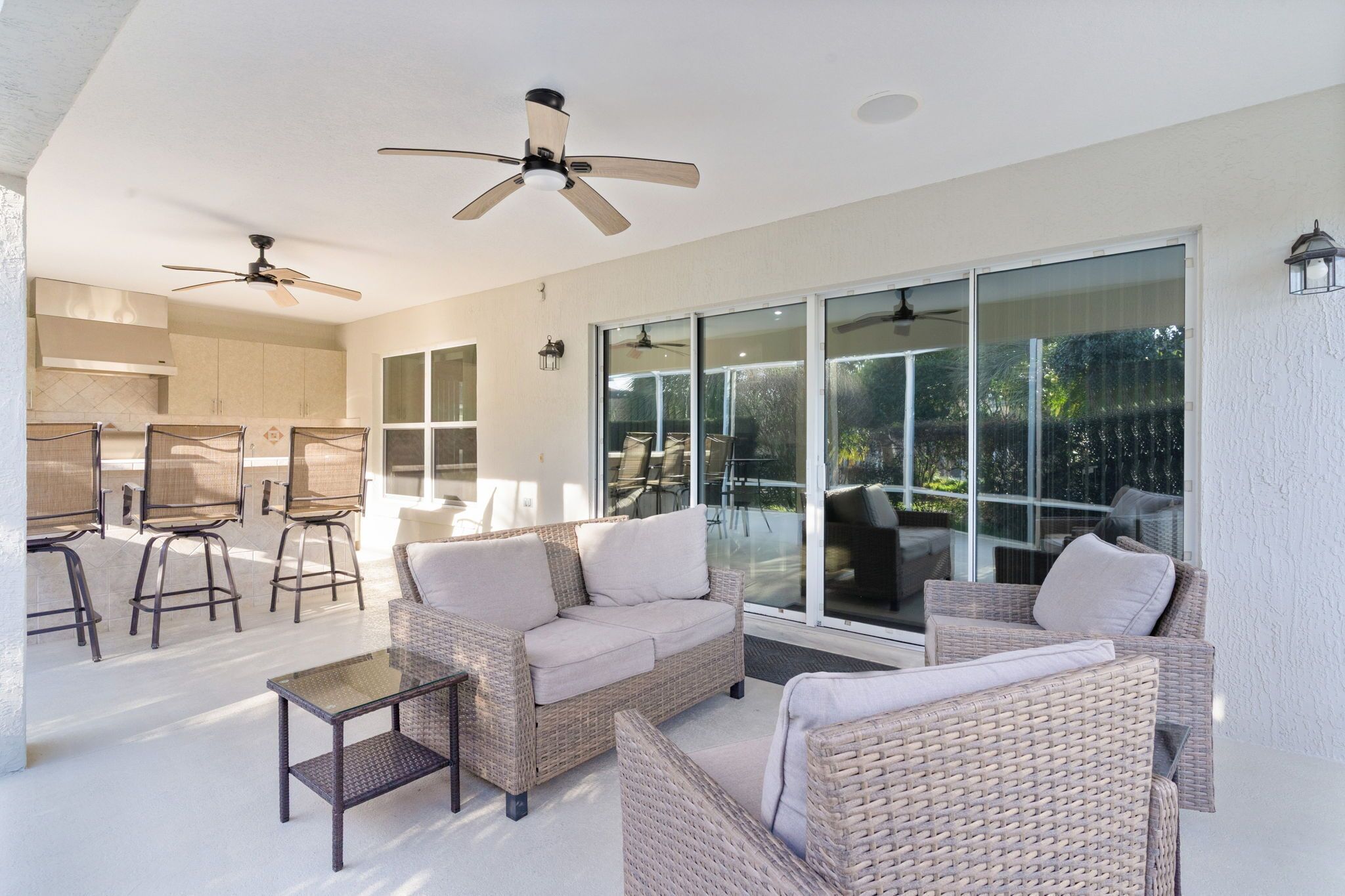 A spacious patio with wicker furniture, ceiling fans, and large sliding glass doors leading to a backyard.