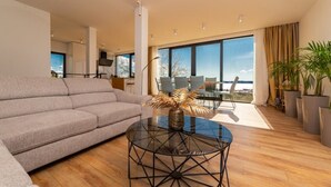 A modern living room with a grey sofa, a glass coffee table, and a view of the outdoors through large windows. - Dalmatian Oasis Luxury Villa (Kaštel Lukšić)