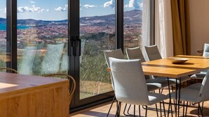 A dining area with a table and chairs, large windows with a view of a cityscape and mountains. - Dalmatian Oasis Luxury Villa (Kaštel Lukšić)