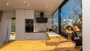 A modern kitchen with a wooden countertop, built-in appliances, and a large window offering a view of trees. - Dalmatian Oasis Luxury Villa (Kaštel Lukšić)