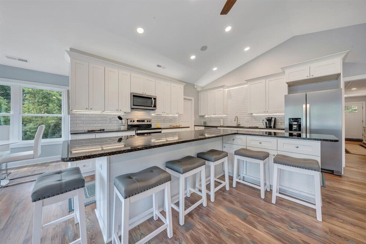 A modern kitchen with white cabinetry, a large island with bar stools, a built-in microwave, and a stainless steel refrigerator.
